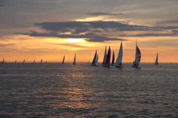 Sailboats on the sea at sunset with a bridge in the background.