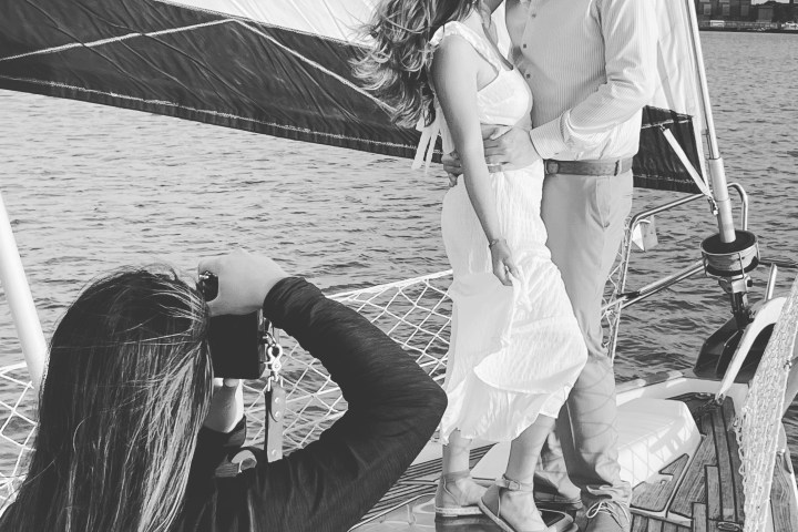 Photographer captures couple embracing on a sailboat with sails unfurled.