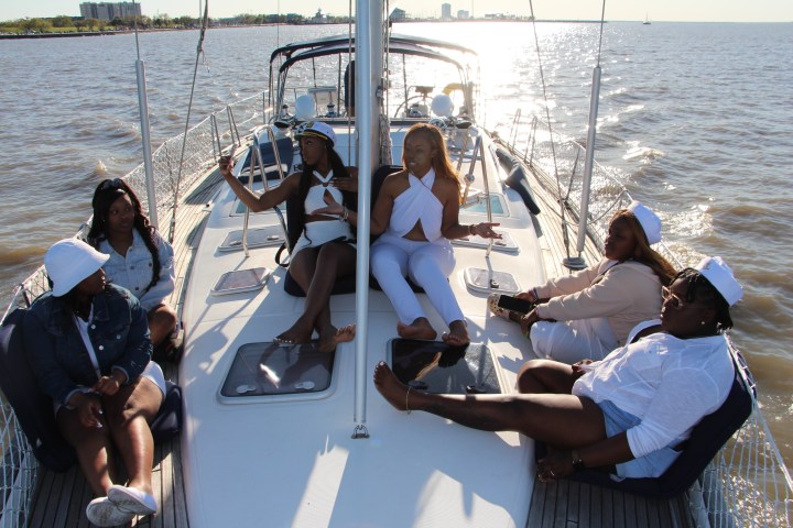 Six people relaxing on a sailboat deck, enjoying a sunny day on the water.