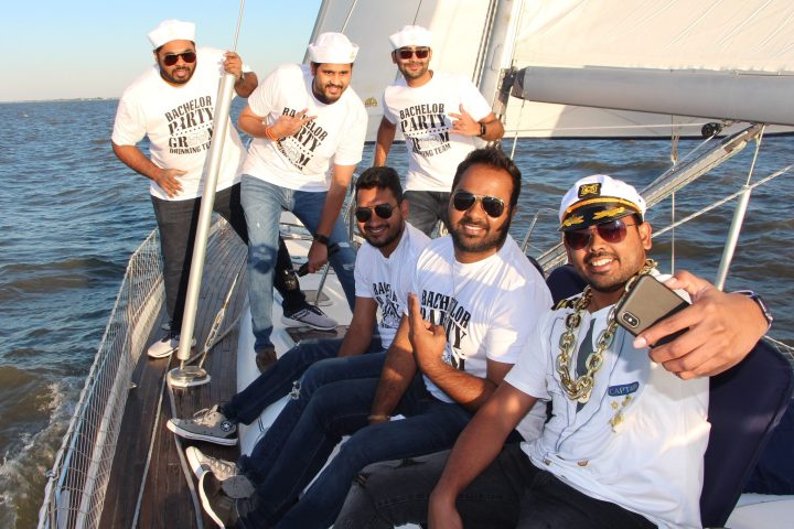 Group of men wearing sailor hats and t-shirts posing on a sailboat during a bachelor party.