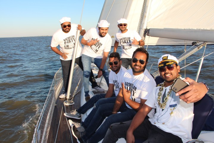 Group of men wearing sailor hats and t-shirts posing on a sailboat during a bachelor party.