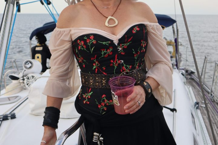 Smiling woman in pirate-themed attire on a sailboat holding a pink drink.