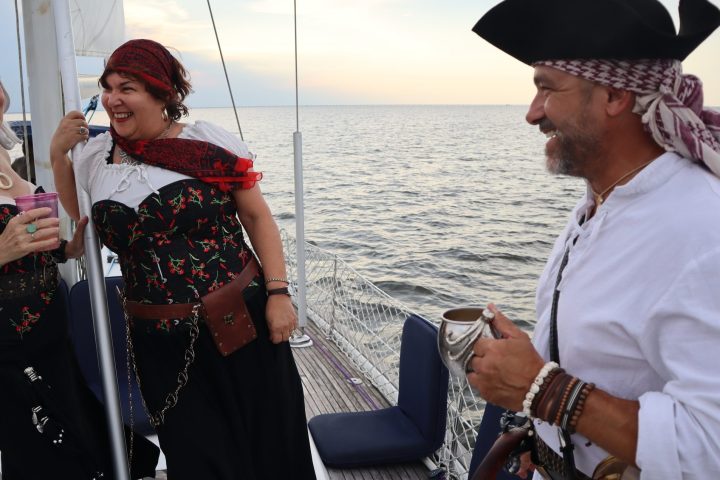 Three people in pirate costumes laughing on a boat at sea.