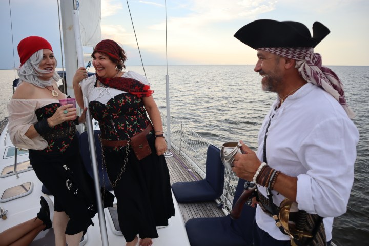 Three people in pirate costumes laughing on a boat at sea.