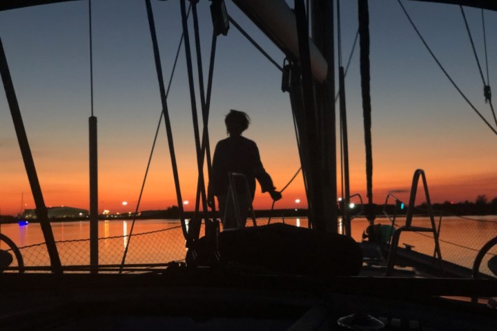 Silhouette of person on a boat at sunset, with orange sky and calm water.