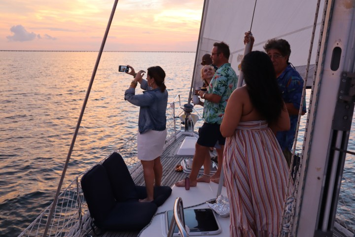 Group of people enjoying sunset on a sailboat, one taking a photo.