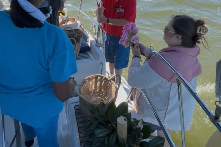 People on a boat with flowers and baskets, ocean and city skyline in the background.