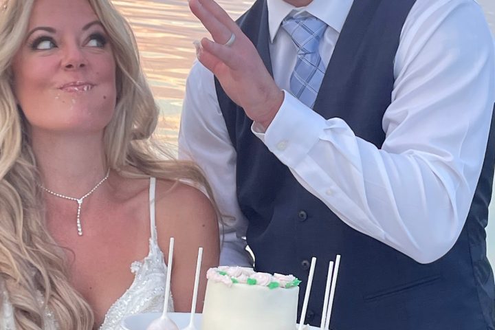 Couple smiling by a small cake with lollipops on a boat at sunset.