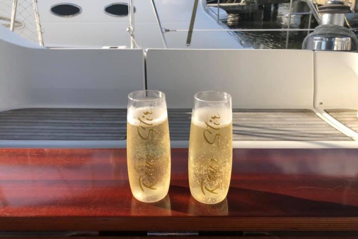 Two champagne glasses on a boat table with a marina background.
