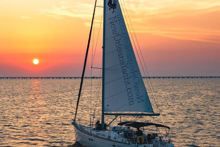 Sailboat on water during sunset with colorful sky and distant bridge.