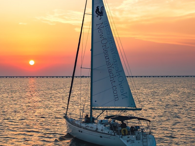 Sailboat on water during sunset with colorful sky and distant bridge.