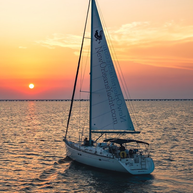 Sailboat on water during sunset with colorful sky and distant bridge.