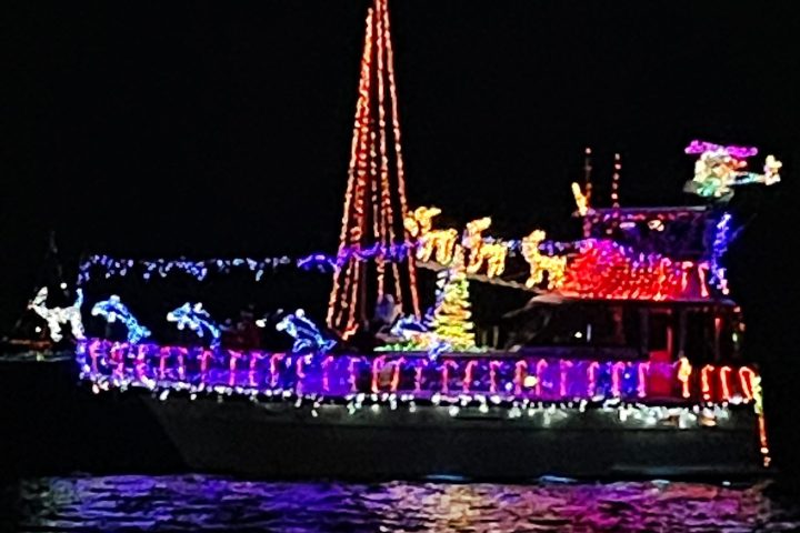 Boat adorned with colorful Christmas lights on water at night.