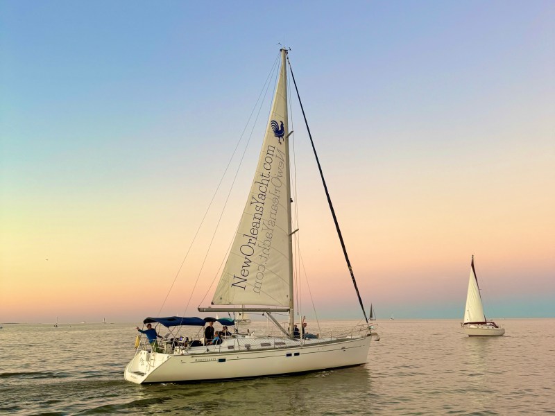 Two sailboats on calm water with a gradient sunset sky in the background.