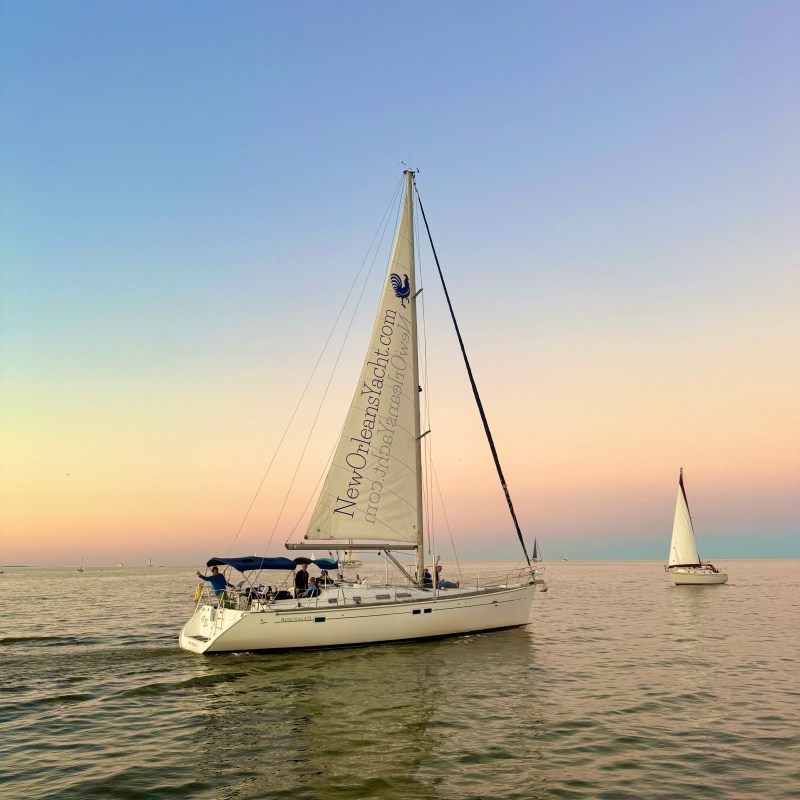 Two sailboats on calm water with a gradient sunset sky in the background.