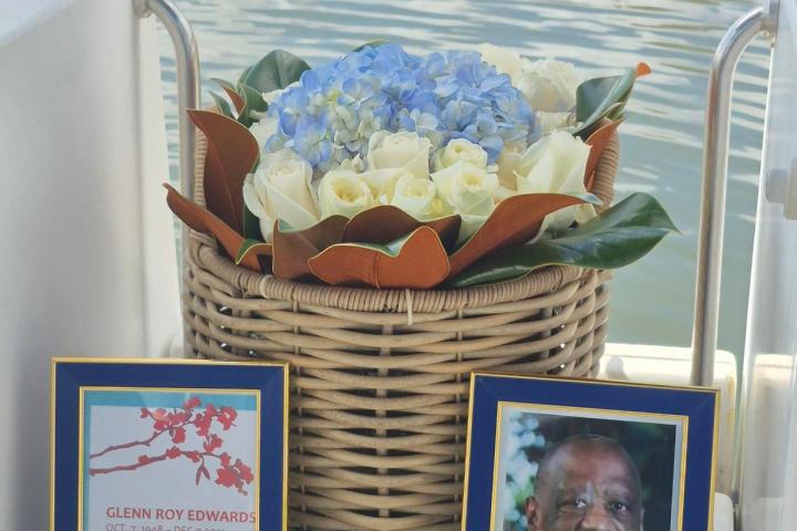 Memorial display on a boat with flowers and framed photo near water.