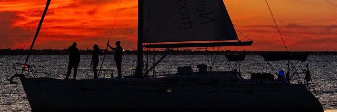 Silhouetted sailboat on water at sunset with vibrant orange sky.