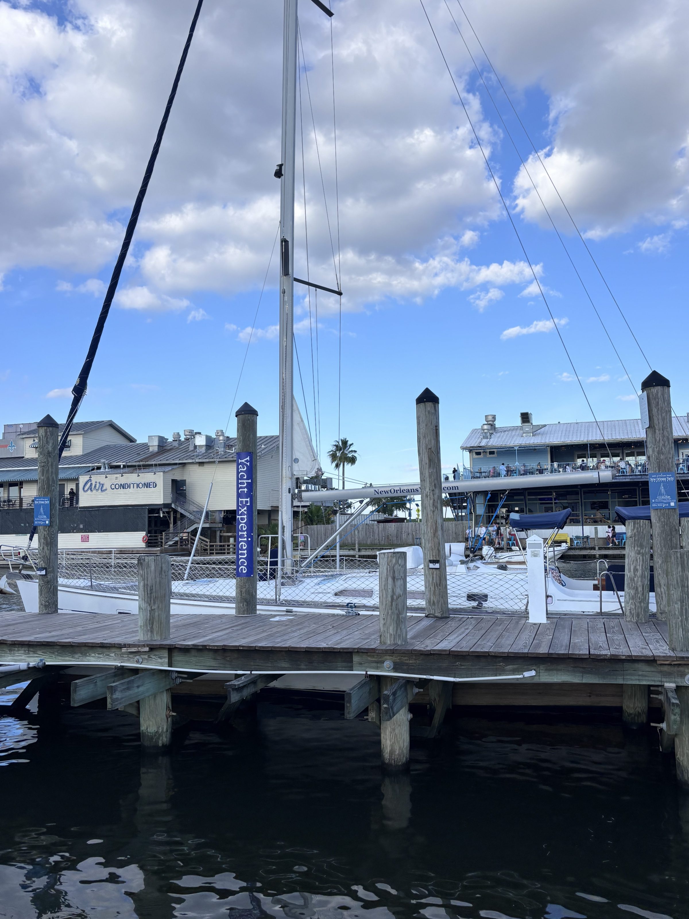 Dock with sailboats and a 'Yacht Experience' sign, cloudy sky.